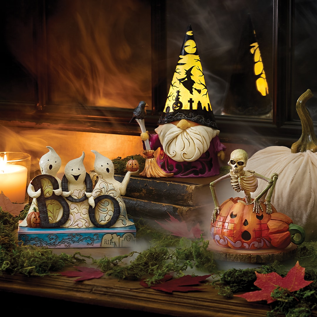 Jim Shore Halloween-themed decorations and figurines including a gnome, skeletons, and ghosts on a table with a candle and leaves.