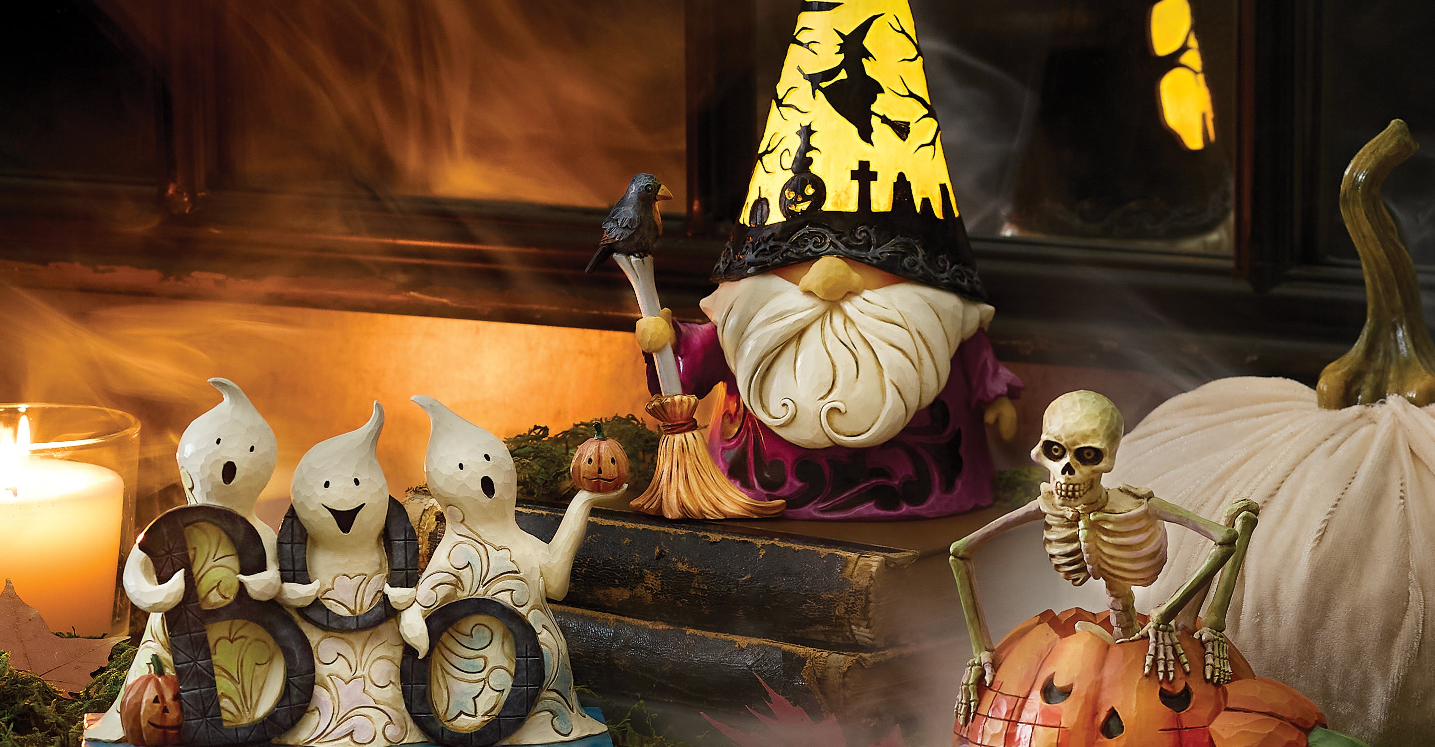 Jim Shore Halloween-themed decorations and figurines including a gnome, skeletons, and ghosts on a table with a candle and leaves.